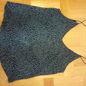 Svart glittrig linnetopp från Sisters Point - Säljer en svart glittrig linnetopp från Sisters Point med smala axelband och ett mönster av silvriga trådar. Toppen har en lös passform och är perfekt för att sticka ut lite extra.