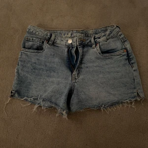Blå jeansshorts med fransig kant från Kappahl  - Säljer ett par klassiska blå jeansshorts från Kappahl. Dem har fransig kant nertill och normal passform. Perfekta för sommaren och enkla att matcha med olika toppar. Skulle säga att dem passar någon som har storlek xs.