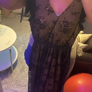 Svart långklänning med spets från Vila - Svart långklänning från Vila med transparent spets och blommigt mönster. Djup v-ringning och korta ärmar i spets. Klänningen har markerad midja och är helfodrad undertill. Perfekt för dig som vill sticka ut.