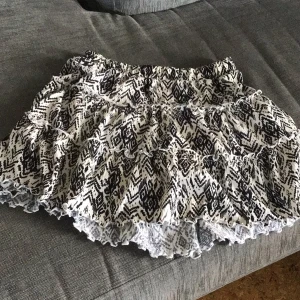 Mönstrad volangkjol från Lindex - Supersöt kortkjol från Lindex med svartvitt mönster och flera volanger. Kjolen har resår i midjan och är perfekt för dig som gillar en lekfull och trendig stil.