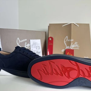 Christian Louboutin Skor - Säljer ett par marinblåa sneakers från Christian Louboutin med klassisk röd sula och diskret broderad logga på hälen. Skorna har snörning och är tillverkade i mocka med en rund tå. Perfekta för dig som vill ha något stilrent men ändå unikt.
