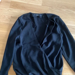 Svart omlottopp från Bik Bok - Svart omlottopp från Bik Bok med lång ärm och djup v-ringning. Tunnare material och stilren design som passar perfekt till många olika outfits.