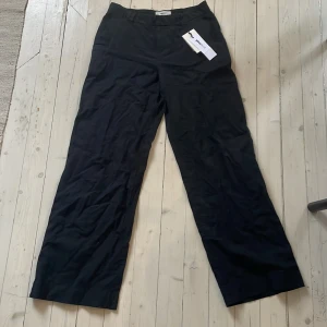 Svarta vida linnebyxor - Svarta byxor i linneblandning med vid passform. Klassisk design med normal midja och raka, vida ben. Perfekta för en stilren och avslappnad look.