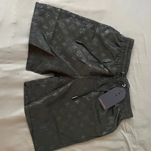 Svarta Louis Vuitton shorts med monogram - Snygga svarta shorts från Louis Vuitton med klassiskt monogrammönster över hela tyget. Shortsen har elastisk midja med snörning och innerfoder i mesh. Perfekta för sommaren och har en modern, normal passform.