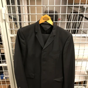 Svart kostym från Tiger of Sweden - Klassisk svart kostym från Tiger of Sweden med kavaj och matchande byxor. Kavajen har smal krage, tre knappar och flera fickor. Perfekt för formella tillfällen och stilrena outfits.