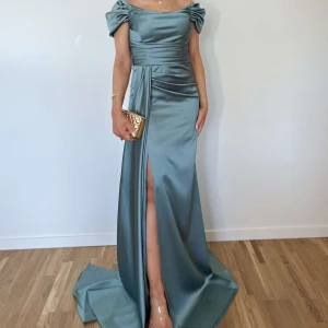 Turkosgrön axelbandslös långklänning i satin - Turkosgrön klänning storlek 34/36, använd i några timmar. Pris 1300kr. Elegant ljusblå långklänning i satin med offshoulder och hög slits framtill. Klänningen har draperad midja och vacker glansig yta, perfekt för speciella tillfällen. Bär den med klackar och en snygg clutch för en stilren look.