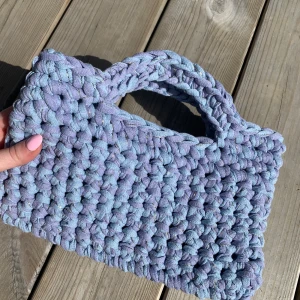 Handgjord virkad handväska - Superfin handväska i lila och blå nyans. Väskan har ett rektangulärt format och inbyggda handtag. Väskan är lila, blå och har även en tråd av guld som löper genom hela väskan. Mått: 26cm bred, 16cm hög