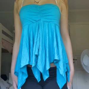  Vintage turkos asymmetrisk kjol  - Säljer en vintage turkos kjol med asymmetrisk och vågig nederkant. Kjolen har en bred midjeresår och är tillverkad i ett mjukt, lätt material som ger ett snyggt fall. Perfekt för dig som vill ha en färgstark och unik look. Går att användas som en tröja och kjol 