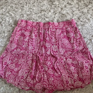 Kjol från Zara - Säljer en kjol ifrån Zara med blommigt mönster och resår i midjan. Shortsen har snörning framtill och är perfekta för varma dagar. Lätta och luftiga med avslappnad passform.