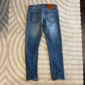 Blå jeans från Jacob Cohën - Snygga blå jeans från Jacob Cohën med klassisk femficksdesign och orange kontrastsömmar. Jeansen har en rak passform och är tillverkade i mjukt denimtyg. Bakfickan har en unik söm och bak finns en orange patch med ett J. Perfekta för en avslappnad stil.
