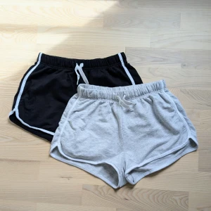 2-pack mjukis shorts med snörning - Två par mjukis shorts, ett par svarta med vita detaljer och ett par ljusgrå. Båda har elastisk midja och snörning framtill. Perfekta för träning eller chill dagar. Köp en för 50 kr. Använd en gång var nästintill nytt skick. Se andra bild för att se hur den ser ut på notera att den är alldeles för liten.