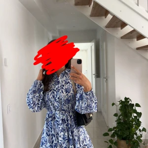 Blåvit blommig kortklänning med knyt - Superfin kortklänning i vitt och blått med blommigt mönster. Klänningen har långa puffärmar, markerad midja med knytband och klassisk krage. Perfekt för en fräsch och trendig look i sommar eller vår. Klänningen är använd endast 3 ggr. 