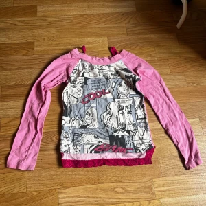 Rosa långärmad tröja med serietryck - Cool långärmad tröja från KappAhl med rosa ärmar och serietidningsinspirerat tryck i svart, vitt och grått framtill. Nedtill finns en snygg rosa spetskant. Barnstorlek man passar xs, eventuellt s
