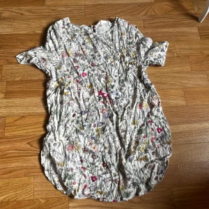 Blommig tunika från H&M - Supersöt tunika från H&M i vitt med  blommönster. Den har korta ärmar och rund halsringning. 🩷😊