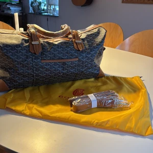 Goyard weekendbag - Snygg och rymlig weekendbag från Goyard med klassiskt grafiskt mönster i svart och grått. Väskan har bruna skinnhandtag, detaljer och medföljande axelrem. Perfekt för resor och har dragkedja upptill. Kommer med original dustbag. Hör av vid minsta intresse!