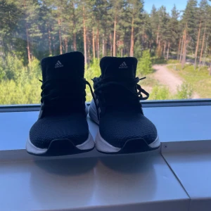 Svarta Adidas sneakers strl 37 1/3 - Svarta Adidas sneakers med vita ränder på sidorna och vit sula. Ovandelen är i mesh för bra andningsförmåga och skon har klassisk snörning. Perfekta för dig som gillar sportig stil och vill ha bekväma skor till vardagen.