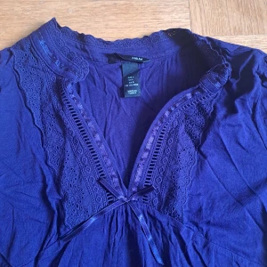 Mörklila blus med spets från H&M - Supersöt mörklila blus från H&M med broderade spetsdetaljer längs v-ringningen och ett litet knytband framtill. Blusen har trekvartsärm och är gjord i mjuk bomull. .