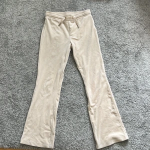 Beiga mjukisbyxor från Gina Tricot - Supermjuka beiga mjukisbyxor från Gina Tricot med bootcut-ben och snörning i midjan. Byxorna har två bakfickor och är gjorda i ett skönt material som känns riktigt chill. Perfekta för en avslappnad look.