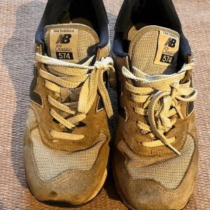 Beige New Balance 574 sneakers -  Säljer ett par New Balance som är använda, men fortfarande funkar bra. Har försökt tvätta dem lite så de ser helt okej ut. Storlek 44, men skulle säga att de passar bättre som 43. Perfekta som vardagsskor eller att ha som slit-och-släng.