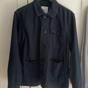 Svart overshirt från Adnym Atelier - Säljer en svart overshirt från MQ nypris är 899 och har inga defekter utan säljs då jag tycker att den är för liten för mig! (Därav de ganska höga priset) Atelier med klassisk krage, tre stora fickor framtill och knäppning med knappar. Jackan har en clean och stilren look som passar perfekt till jeans eller chinos. Materialet är mjukt och känns skönt mot huden. Jackan passar perfekt nu till sommaren! Hör av er vid intresse! 