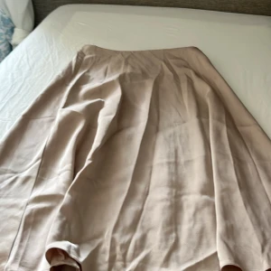 Beige långkjol från SHEIN, XS - Beige långkjol från SHEIN i flowy modell med lätt glansigt tyg. Kjolen har en enkel och stilren design utan mönster, perfekt för dig som gillar en clean look. Stängs med dragkedja i sidan och har en mjuk, skön känsla mot huden.