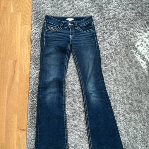 Blå bootcut jeans med kontrastsömmar - Snygga blå jeans med bootcut-modell och markerade kontrastsömmar. Klassiska femficksdetaljer och coola ficklock med knapp bak. Jeansen har låg midja och är tillverkade i stretchig denim för en bekväm passform.