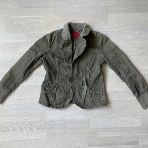 Jacka från Esisto Conbipel - Snygg jacka från Esisto Conbipel med coola detaljer som ribbade muddar, markerad midja och stora fickor framtill. Jackan har en klassisk krage i manchester och stängs med knappar. Perfekt för dig som gillar en avslappnad men stilren look.