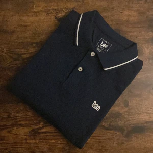 Lee-långärmade piké - Mörkblå långärmad pikétröja från klassiska Lee. Perfekt balans mellan casual och uppklätt – funkar lika bra till jeans som chinos. Skön passform i storlek Small, med mjukt material och stilren knappkrage. Diskret Lee-logga på bröstet ger ett tidlöst uttryck. Ett måste i garderoben för dig som gillar clean och avslappnad stil.  Skick: Mycket bra Storlek: Small Färg: Mörkblå Märke: Lee