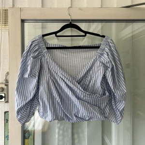 Randig omlottblus från Gina Tricot - Supersöt blus från Gina Tricot med blåvita ränder. Omlottmodell med djup v-ringning och puffiga trekvartsärmar. Storlek 36. (I mycket fint skick, använd några gånger)