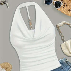 Vit halterneck topp med hjärtdetalj - Supersnygg vit halterneck topp med draperad front och unik guldfärgad detalj med hjärtan och glittrande stenar i mitten. Toppen är ärmlös och har en smickrande passform, perfekt till jeans eller kjol för en trendig look.