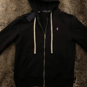 Polo Ralph Lauren Hoodie - Svart hoodie från Polo Ralph Lauren med vit logga🐎 Hoodien är sprillans nytt skick och har kvar Tags 🏷️, Hoodien är i storlek L  men kan även passa M beroende på hur du vill att den ska sitta🙌                        Priset kan diskuterat så tveka inte!!!                 Frågor, bilder, och passform är bara och kontakta Mig🙌