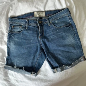 Blå jeansshorts - Snygga blå jeansshorts från Bershka med klassisk femficksdesign och råa, fransiga kanter. Shortsen har normal passform och kan bäras både med upprullade eller raka ben. Perfekta för en avslappnad sommarstil