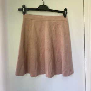 Ljusrosa kjol i mockaimitation H&M - Supersöt ljusrosa kjol från H&M i mjuk mockaimitation. Kjolen är A-linjeformad, har dragkedja och knapp framtill och är tillverkad i polyester med lite stretch. Perfekt för dig som gillar en feminin och stilren look.