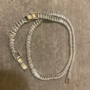 Glittrigt armband med rektangulära stenar - Snyggt armband med glittrande, rektangulära stenar i silverfärg och guldiga detaljer vid låset. Armbandet har en klassisk och stilren design som verkligen fångar ljuset. Perfekt för dig som vill ha något som sticker ut och ger extra bling till din look.