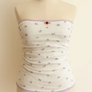 Vit blommig bandeau tubtopp - Supersöt vit bandeau tubtopp med små lila blommor och ljuslila spetskant. Toppen har en liten röd rosett framtill och är ribbad för extra snygg passform. Perfekt för varma dagar eller lager på lager-stil.