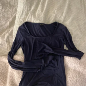 Mörkblå långärmad topp Gina tricot  - Säljer en mörkblå långärmad topp från Gina tricot med rundad, djup urringning. Modellen är slim och sitter snyggt mot kroppen. Tillverkad i mjuk bomull som känns skön mot huden. Perfekt att styla med jeans eller kjol för en clean look.
