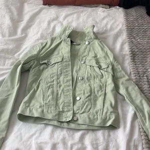 Ljusgrön jeansjacka från H&M Divided XS - Snygg ljusgrön jeansjacka från H&M Divided i storlek XS. Klassisk modell med silvriga knappar framtill, två bröstfickor med lock och lång ärm. Perfekt att slänga över en hoodie eller t-shirt för en chill look.