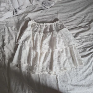 Vit volangkjol från SHEIN - Superfin vit kortkjol från SHEIN med flera lager volanger och smock i midjan. Kjolen är gjord i ett lätt, strukturerat tyg som känns luftigt och passar perfekt till varma dagar. Enkel att matcha med crop tops eller oversized t-shirts. Storlek 10-11y men skulle säga att det är xs, då kjolen är lite stor i storleken. Finns två små fläckar (se bild 4)