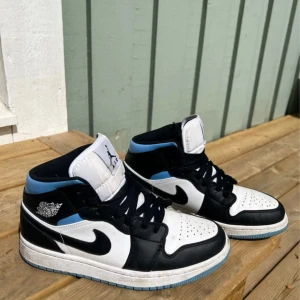 Nike Air Jordan 1 Mid svart/vit/blå - Snygga Nike Air Jordan 1 Mid sneakers i svart, vitt och ljusblått.