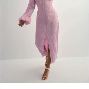 Ljusrosa långklänning med knappar från Nelly  - En rosa långärmad klänning ifrån Nelly med knappar, den är figurformad otroligt fin och avslappnad aldrig använd med prislapp säljer för att jag skulle ha den på ett bröllop men hittat en annan! Nypris 799kr pris kan diskuteras