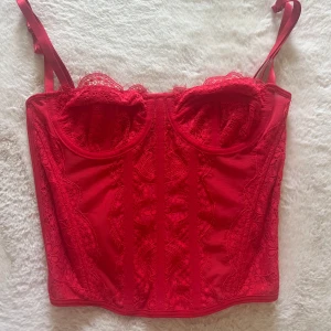 Röd spetskorsett med axelband - Snygg röd korsett med justerbara axelband och fina spetsdetaljer på sidorna i storlek XS.