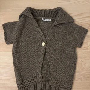 Brun stickad kofta från Zara - Kortärmad slutsåld brun stickad kofta från Zara med stor krage och en unik, ljus knapp framtill. Koftan har ribbade muddar och en loose fit som ger en chill vibe. Perfekt att slänga över en t-shirt eller linne för extra stilpoäng. Skriv för frågor eller flera bilder!