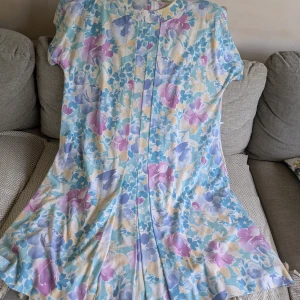 Blommig pastellklänning - Luftig klänning med hög krage i blommigt mönster och med skönt material från Finn Karelia. Klänningen har en dragkedja vid nacken/på övre delen av ryggen. Det finns även hällor i midjan för man kan ha ett tunt skärp. Oklart vad det är för storlek så jag har uppskattat, men den fungerar som nästan vad som helst beroende på hur man vill att den ska sitta!