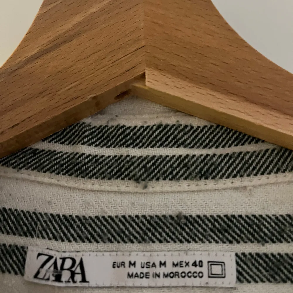 Säljer en stilren randig skjorta från Zara i vitt och grönt. Skjortan har korta ärmar och en klassisk krage. Perfekt för en avslappnad stil. Tillverkad i ett lätt och bekvämt material.. Paidat.