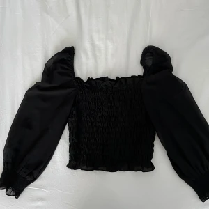 Svart  topp från H&M Divided - Säljer en svart  topp från H&M Divided med  puffärmar och volangdetaljer vid ärmslut och nederkant. Bra skick!