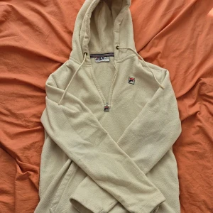 Mjuk FILA hoodie  - Säljer en beige hoodie från Fila med dragkedja och huva. Tröjan har en liten Fila-logga på bröstet och är perfekt för en avslappnad stil. Den är gjord i ett mjukt material som känns skönt mot huden.