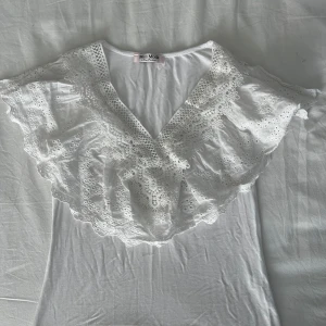 Vit blus från Miss Moda - Säljer en söt vit blus från Miss Moda med v-ringning och spetsdetaljer. Blusen har korta ärmar och ser ut som ett linne bakifrån.