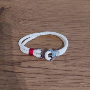 Vitt armband med metallspänne - Snyggt vitt armband med ett unikt metallspänne och en röd detalj. Perfekt för att ge en stilren touch till din outfit.