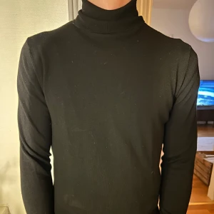 Svart polotröja från Baldini - Snygg svart polotröja från baldini med långa ärmar. Perfekt för kyligare dagar och enkel att matcha med olika outfits. Tröjan har en klassisk design med ribbade muddar vid ärmslut och nederkant.