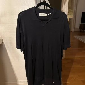 Svart pikétröja från Les Deux - Säljer en stilren svart pikétröja från Les Deux. Tröjan har korta ärmar och en klassisk krage. Perfekt för en avslappnad men ändå uppklädd look. Passar även L/XL då den är stor i passformen